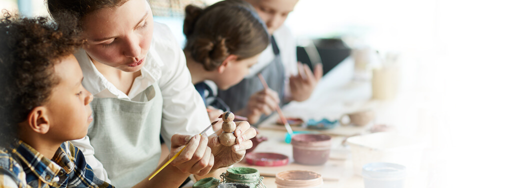 Young teacher showing a pupil a clay item and showing how to paint it