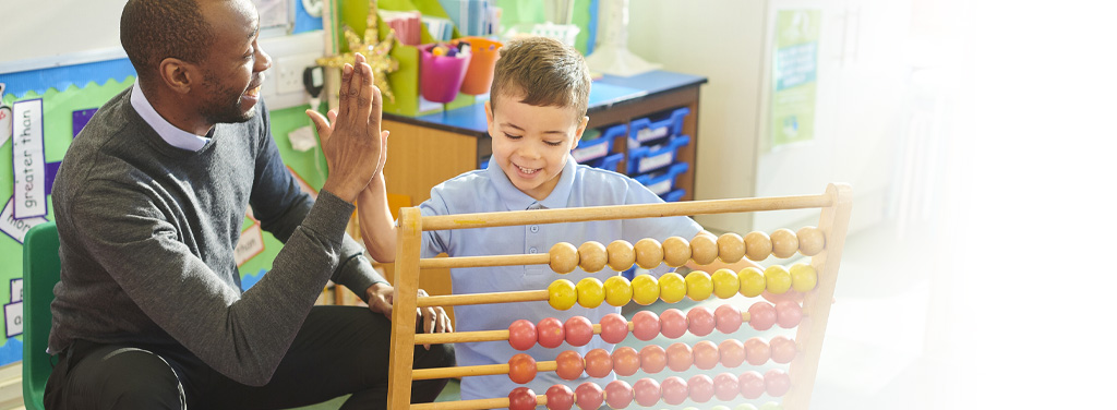 Teacher giving a boy a high five while he works on an abacus